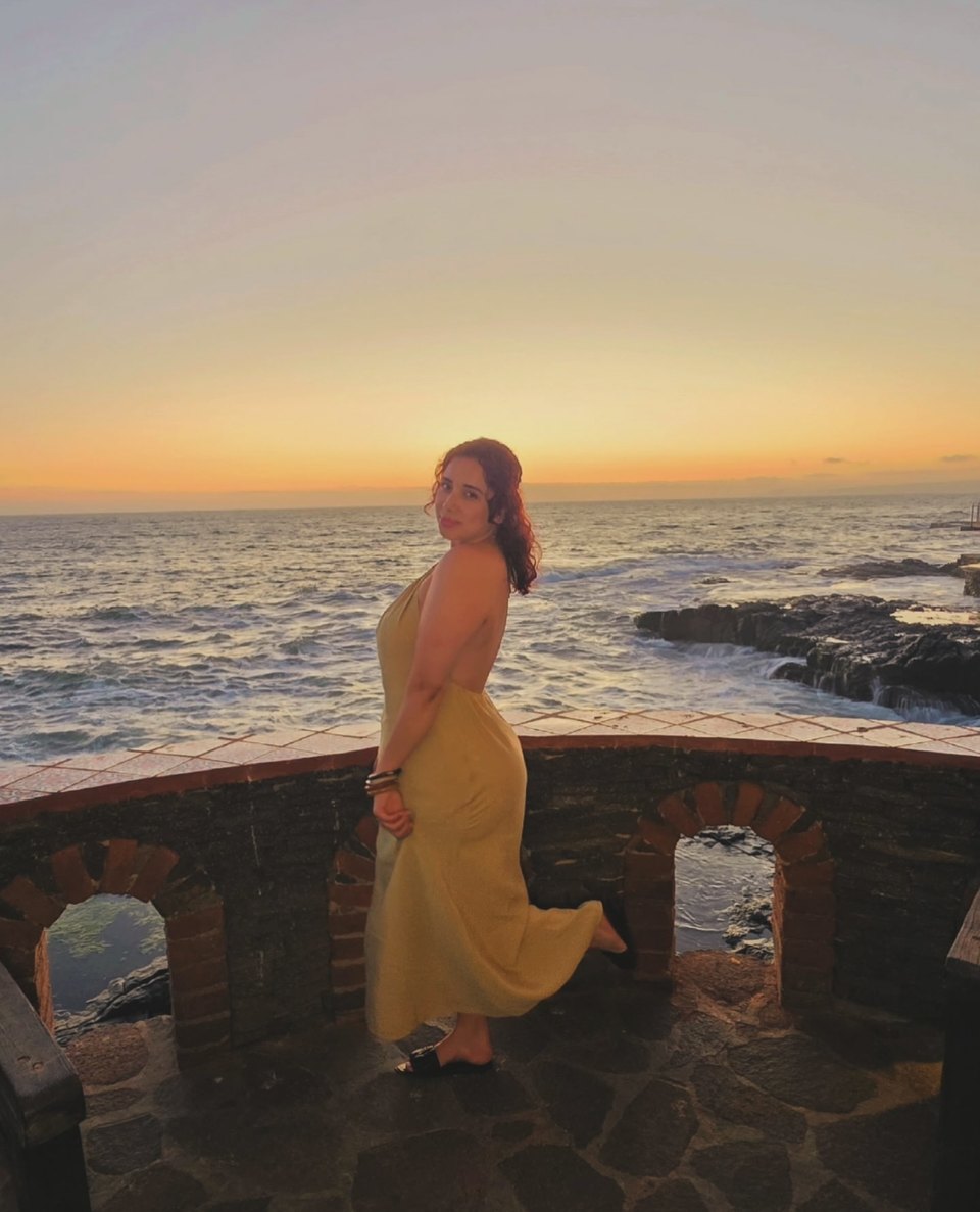 Wendy Estrada in a gold dress beside the ocean at sunset