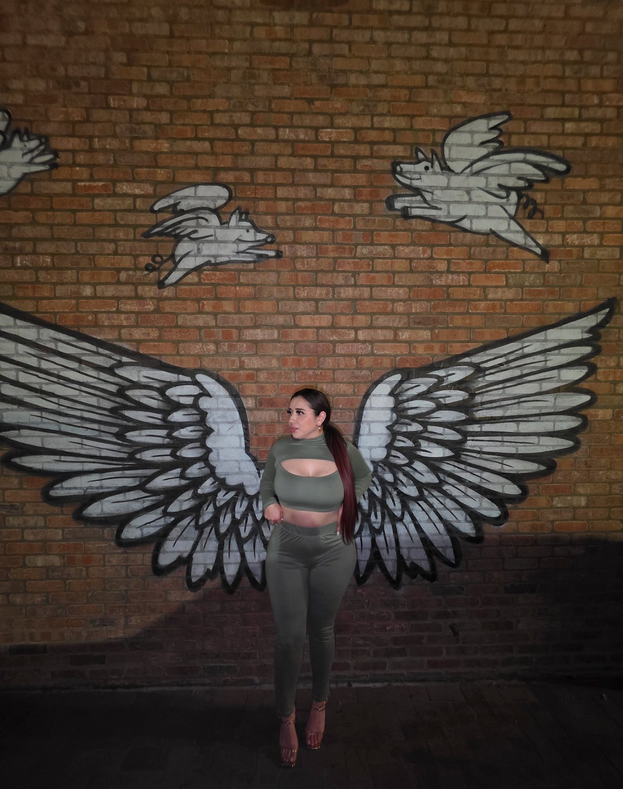 Wendy Estrada standing in front of a brick mural painted with large wings